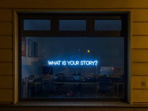 Neon Sign in a window reads What Is your Story